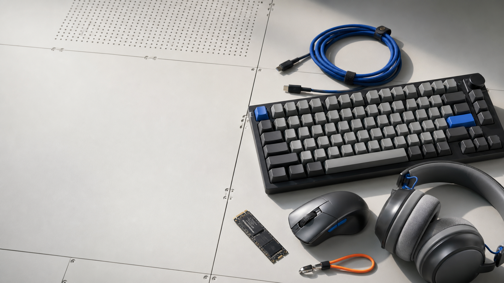 Keyboard, mouse, headphones, SSD, and cables arranged on a modular workbench.